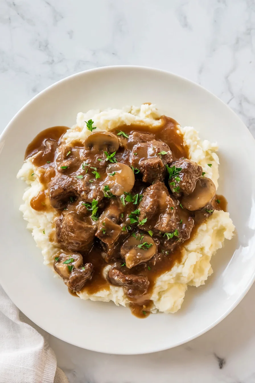 Beef tips with mushrooms and gravy on a plate of mashed potatoes