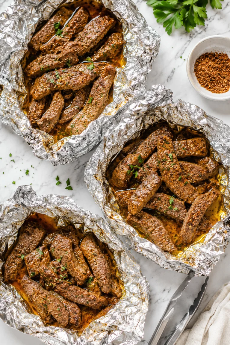 Several open foil packets filled with Cajun-seasoned steak