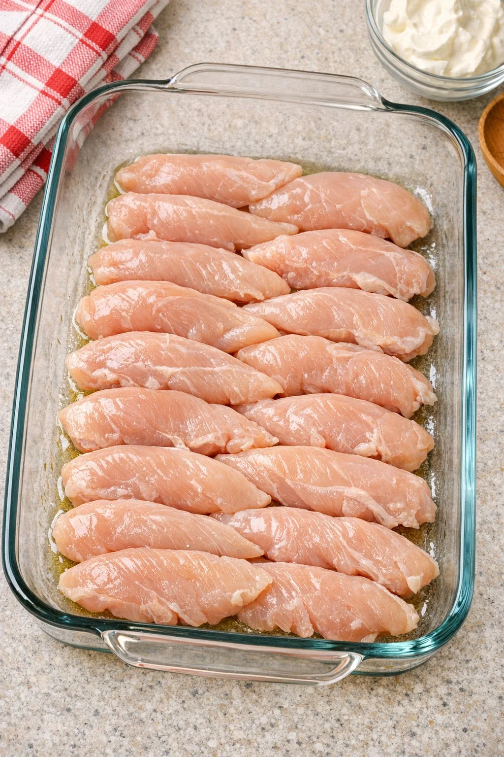 Raw chicken tenderloins arranged in a glass casserole dish