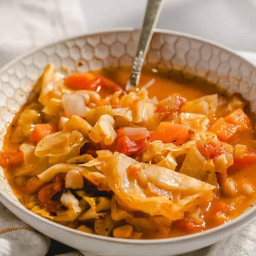 Bowl of cozy cabbage soup with vegetables and herbs for a comforting meal.