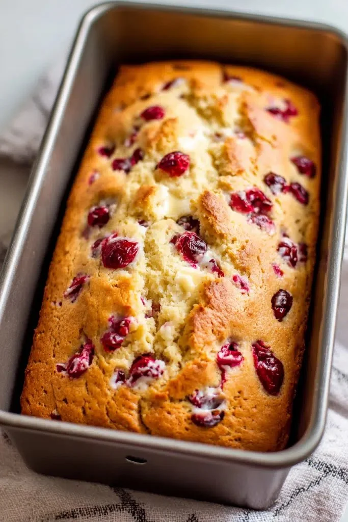 Sliced cream cheese cranberry loaf on a wooden cutting board
