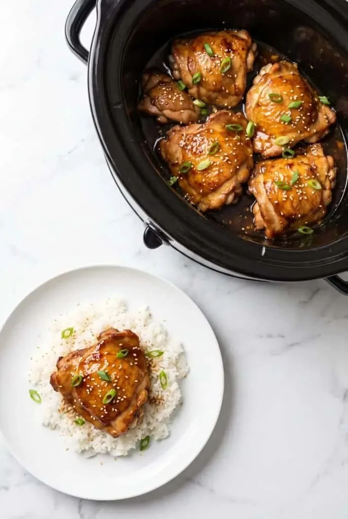 Crockpot teriyaki chicken thighs served on a plate with steamed vegetables.