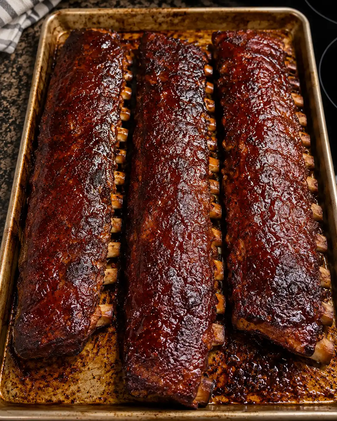 Sticky oven-baked BBQ ribs glazed with rich homemade barbecue sauce on a baking sheet, featuring tender pork ribs with a smoky caramelized finish.