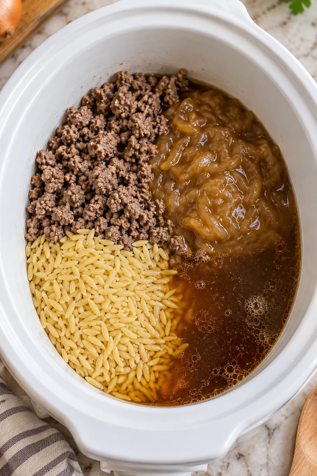 Dry orzo and cooked beef in a slow cooker with French onion soup and broth