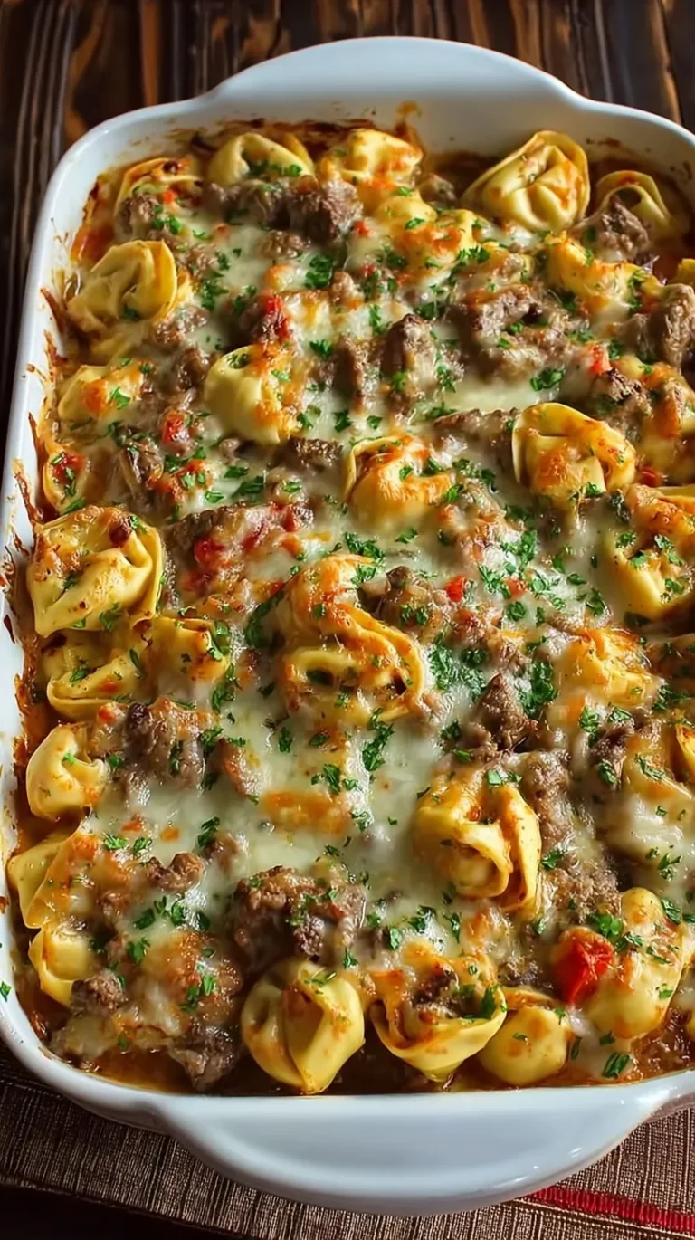 A bubbly Golden Cheese Steak Tortellini Casserole topped with melted provolone cheese and sliced steak.