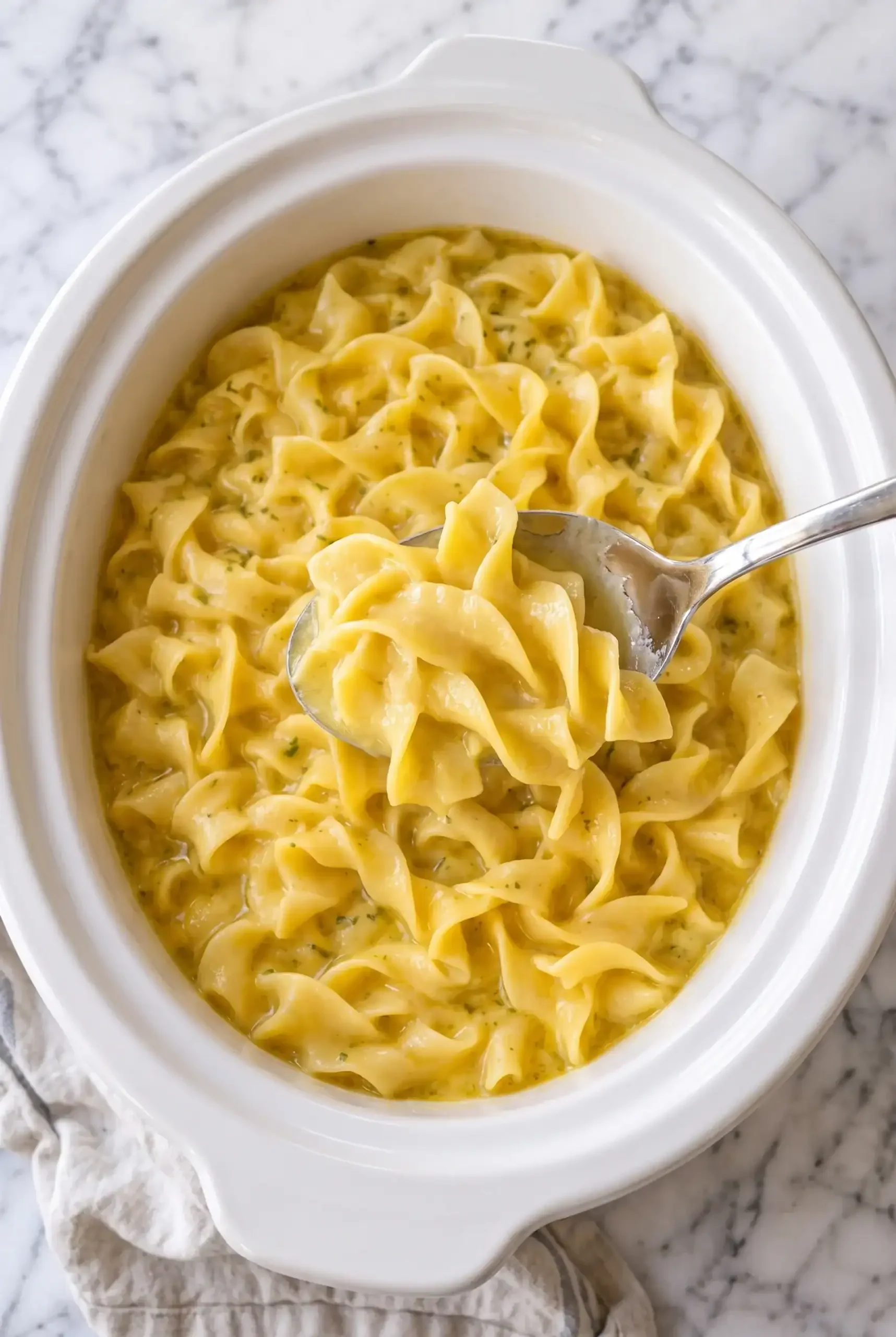 A spoon lifting egg noodles from the slow cooker