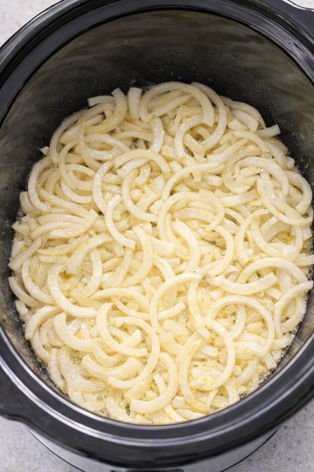 Sliced onions arranged at the bottom of a slow cooker
