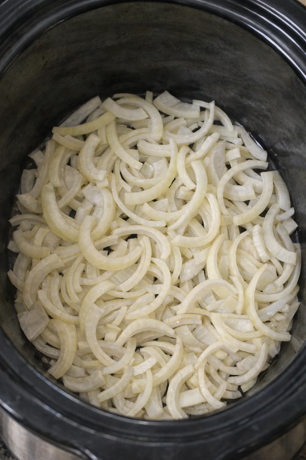 Sliced onions layered across the bottom of a slow cooker