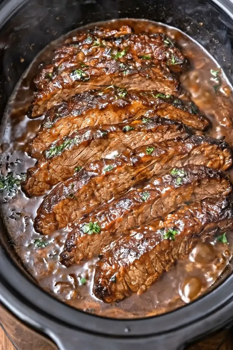 A vertical, close-up shot of a beef brisket slow-cooking in a black ceramic crockpot. The brisket is sliced into thick, succulent pieces that are glistening with a rich, dark brown BBQ sauce. Freshly chopped green parsley is sprinkled over the meat, and the surrounding sauce is bubbling slightly. The beef shows a tender, fibrous texture, indicating it is fork-tender.