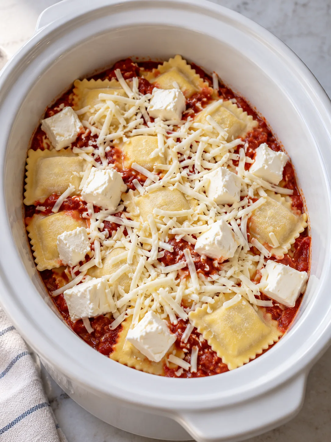 Frozen ravioli layered with marinara cream cheese and mozzarella inside the slow cooker