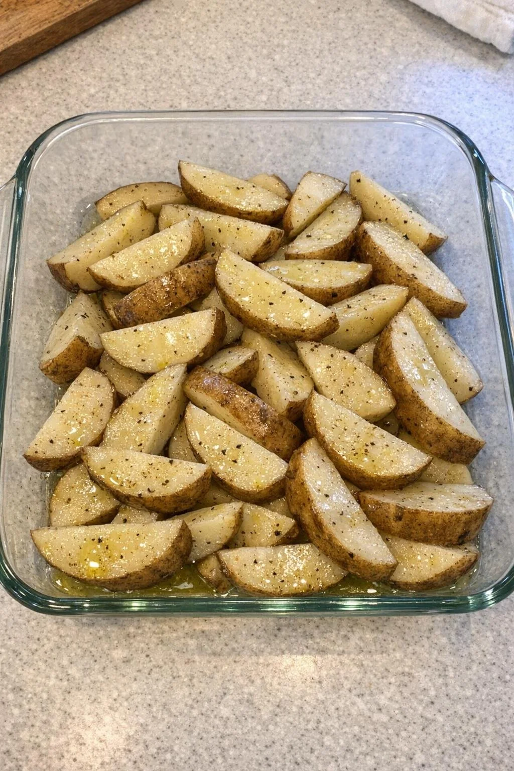 Raw potato wedges tossed with olive oil in a casserole dish