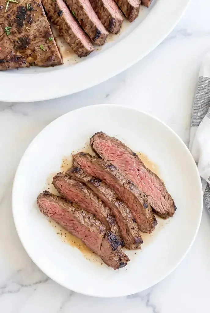 Sliced Tuscan Flank Steak garnished with herbs and served on a platter.